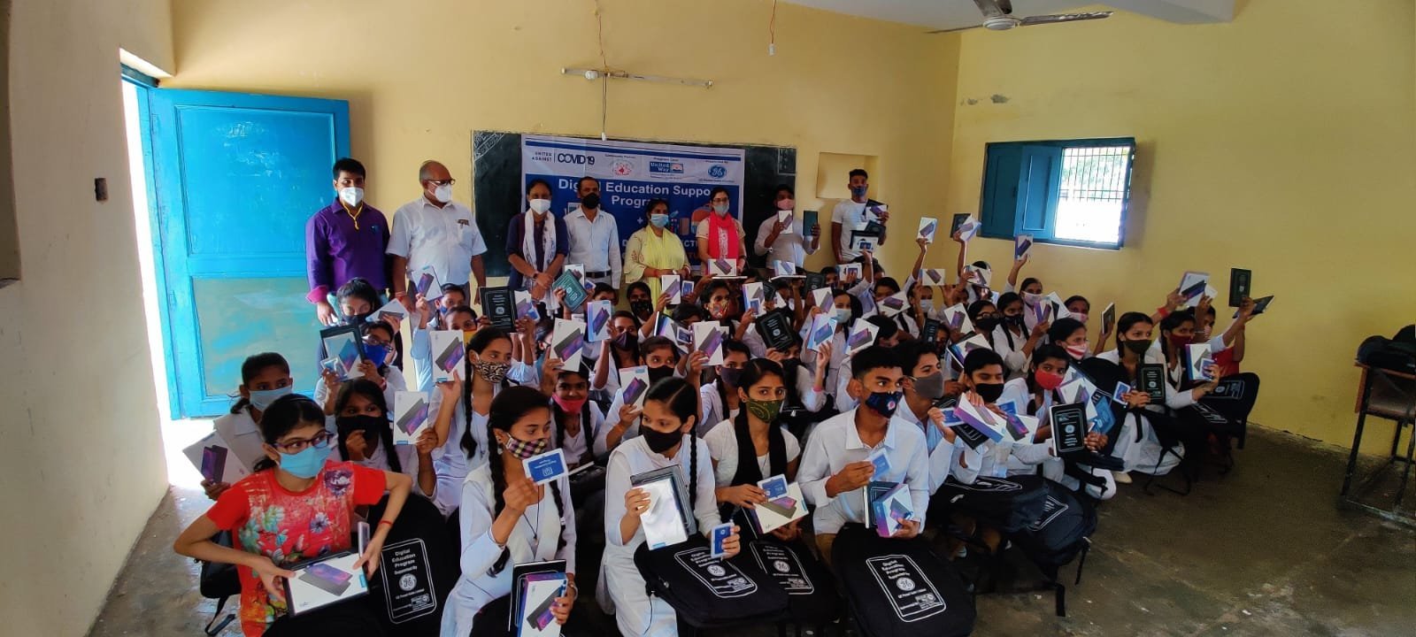 Students hold tablets and learning materials during a CWS distribution event.