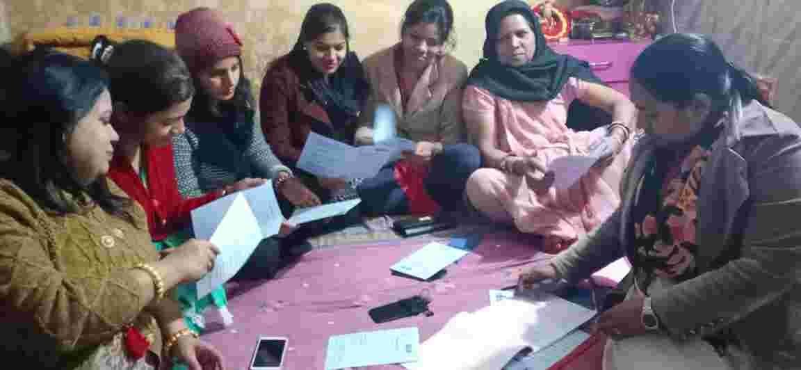 Women seated on the floor together while reviewing papers and notebooks.